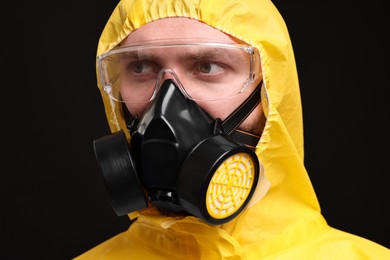 Man wearing protective suit with respirator mask on black background