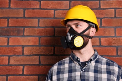 Man in respirator mask and hard hat near red brick wall. Space for text