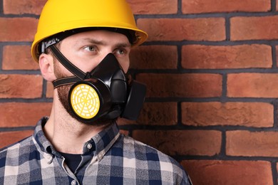 Man in respirator mask and hard hat near red brick wall. Space for text