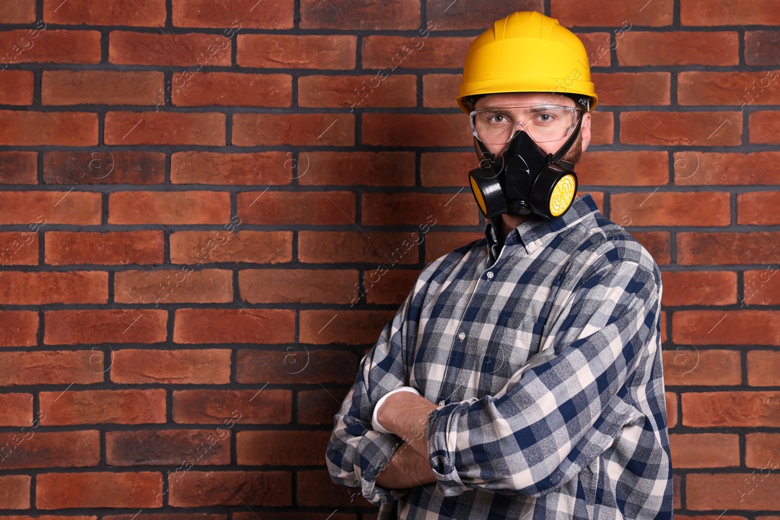 Photo of Man in respirator mask and hard hat near red brick wall. Space for text