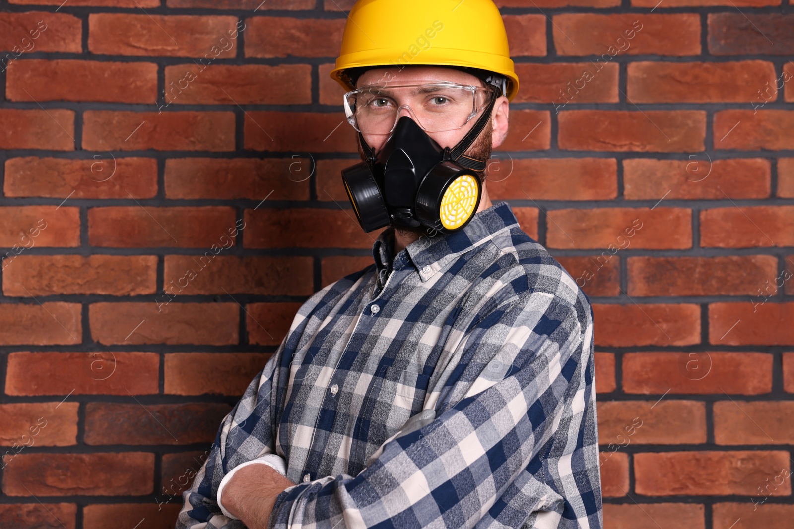 Photo of Man in respirator mask and hard hat near red brick wall