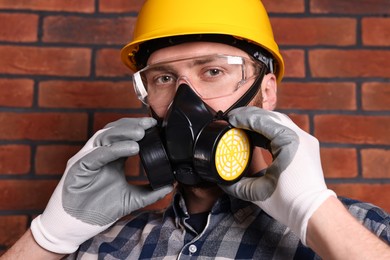 Man in respirator mask and hard hat near red brick wall