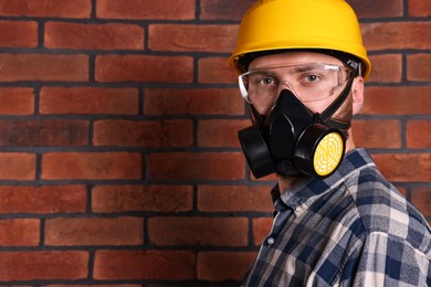 Photo of Man in respirator mask and hard hat near red brick wall. Space for text