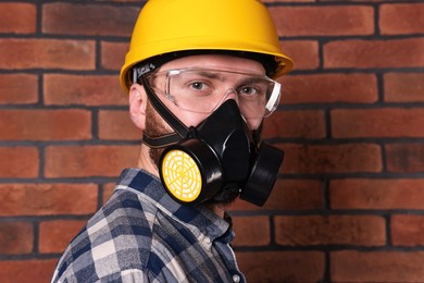 Photo of Man in respirator mask and hard hat near red brick wall
