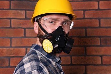 Man in respirator mask and hard hat near red brick wall