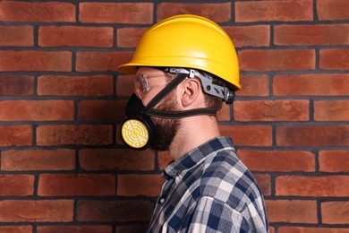 Photo of Man in respirator mask and hard hat near red brick wall