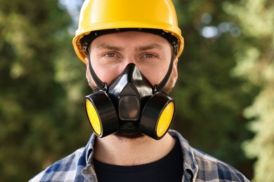 Photo of Man in respirator mask and hard hat outdoors. Safety equipment