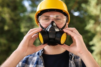 Photo of Man in respirator mask and hard hat outdoors. Safety equipment