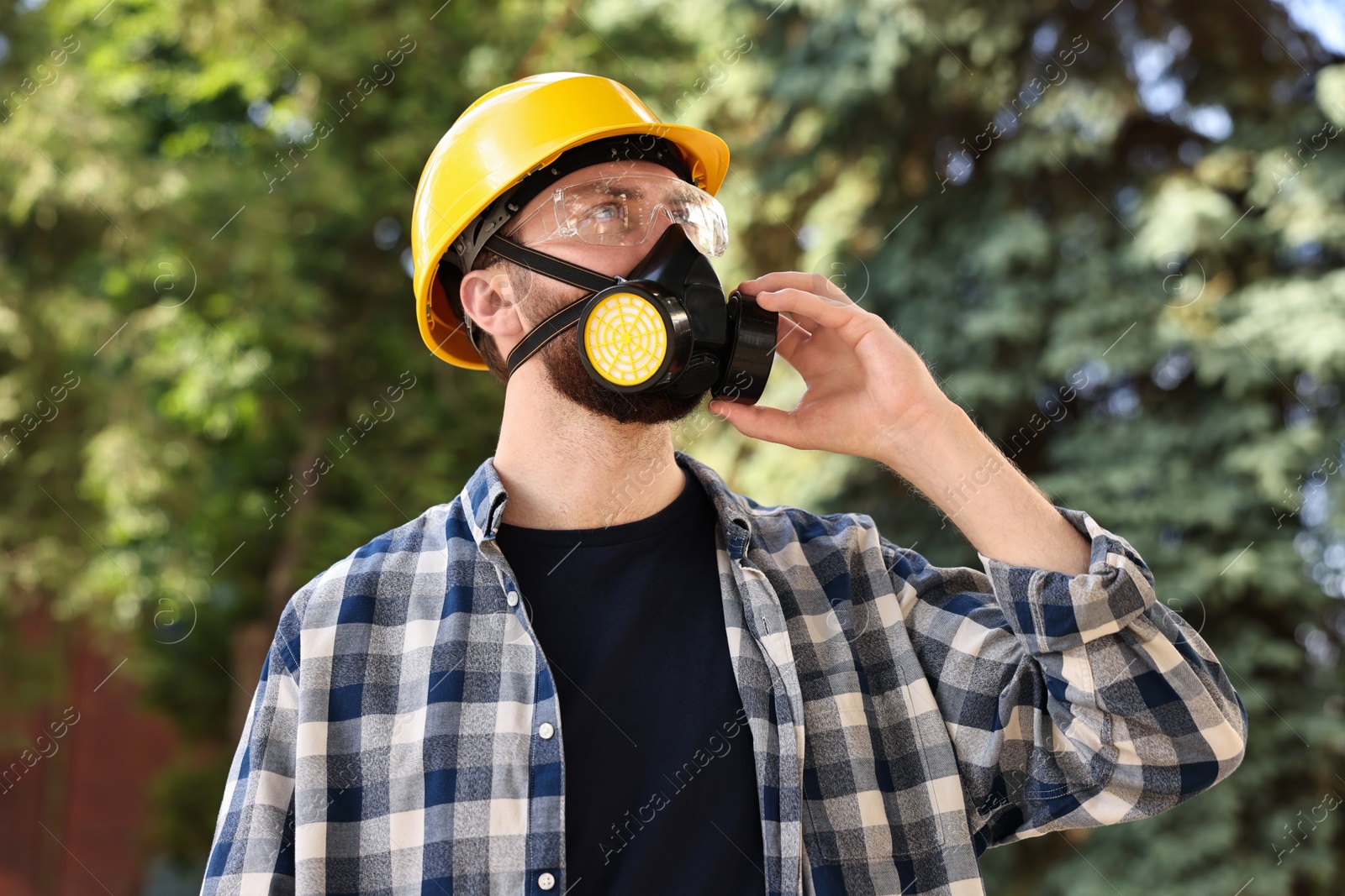 Photo of Man in respirator mask and hard hat outdoors. Safety equipment