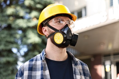 Photo of Man in respirator mask and hard hat outdoors. Safety equipment