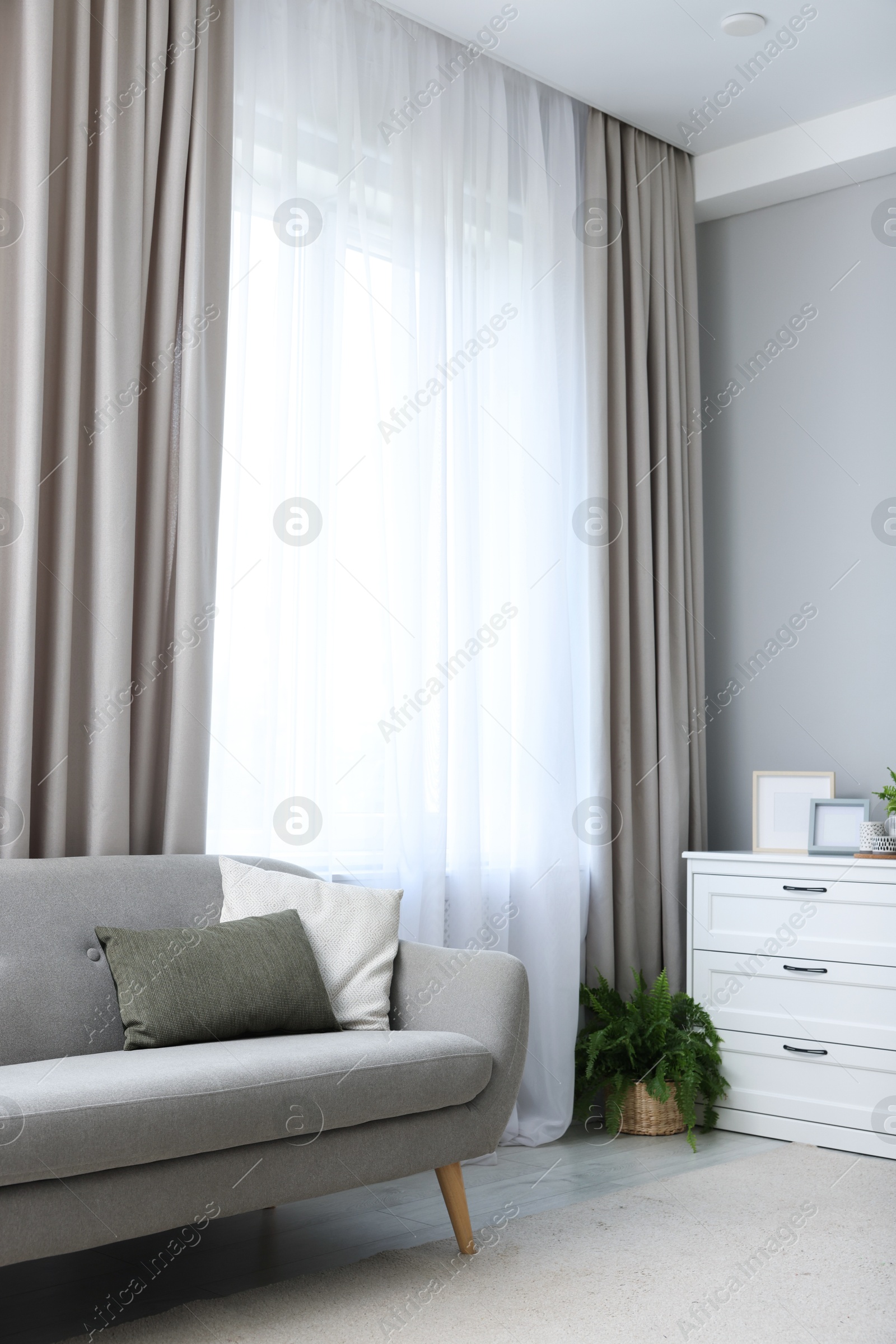 Photo of Comfortable sofa and elegant curtains in living room. Interior design