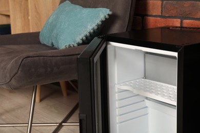 Photo of Empty modern mini refrigerator near chair indoors, closeup