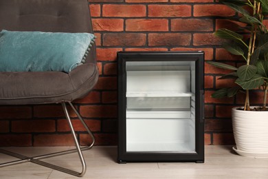 Photo of Empty modern mini refrigerator near chair indoors