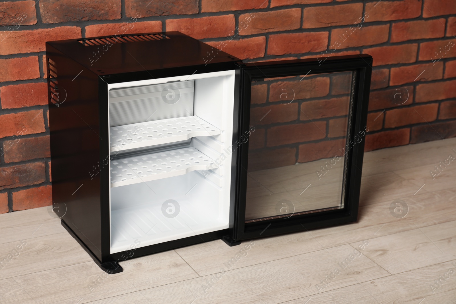 Photo of Empty mini refrigerator near brick wall indoors