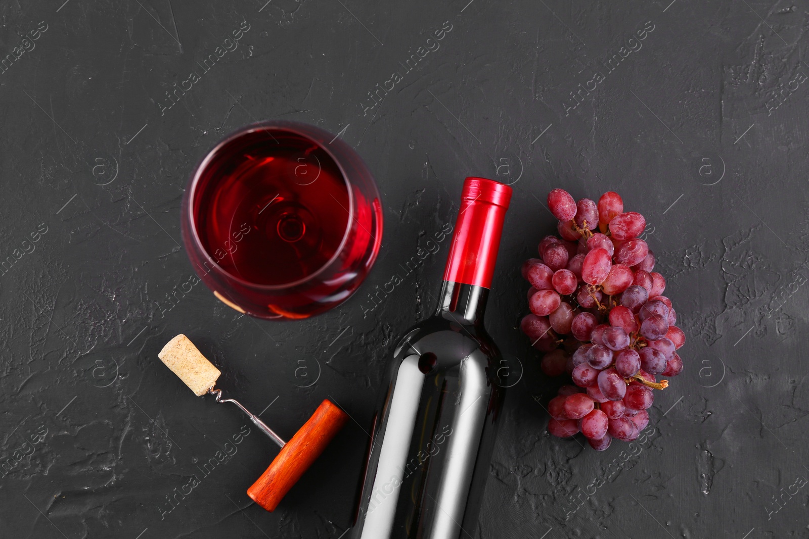 Photo of Corkscrew, glass of wine, bottle and grapes on black table, flat lay