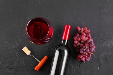 Photo of Corkscrew, glass of wine, bottle and grapes on black table, flat lay