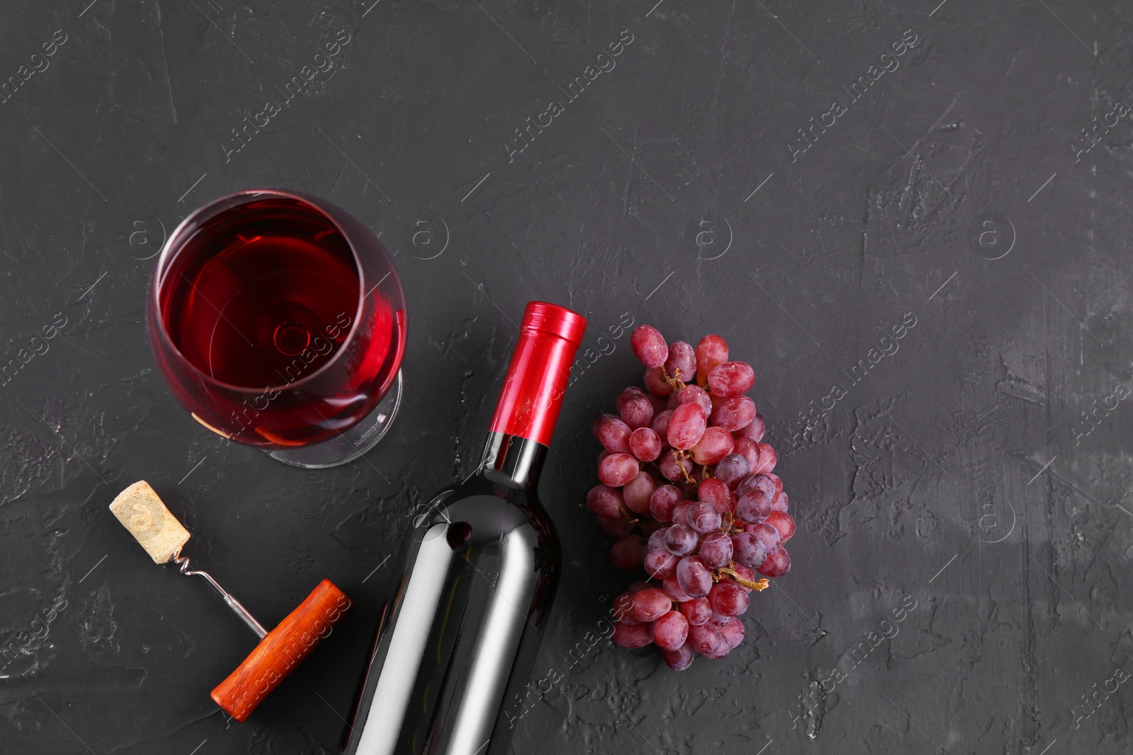 Photo of Corkscrew, glass of wine, bottle and grapes on black table, flat lay. Space for text