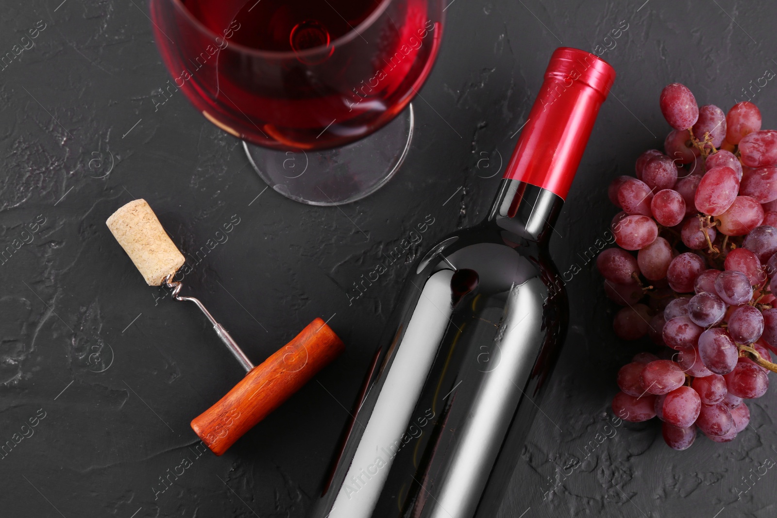 Photo of Corkscrew, glass of wine, bottle and grapes on black table, flat lay