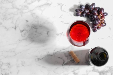 Photo of Corkscrew, glass of wine, bottle and grapes on white marble table, flat lay. Space for text