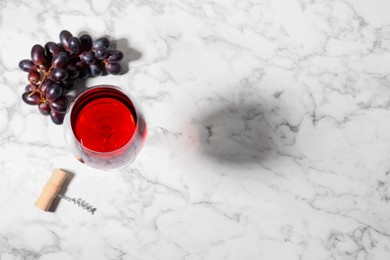 Corkscrew, glass of wine and grapes on white marble table, flat lay. Space for text