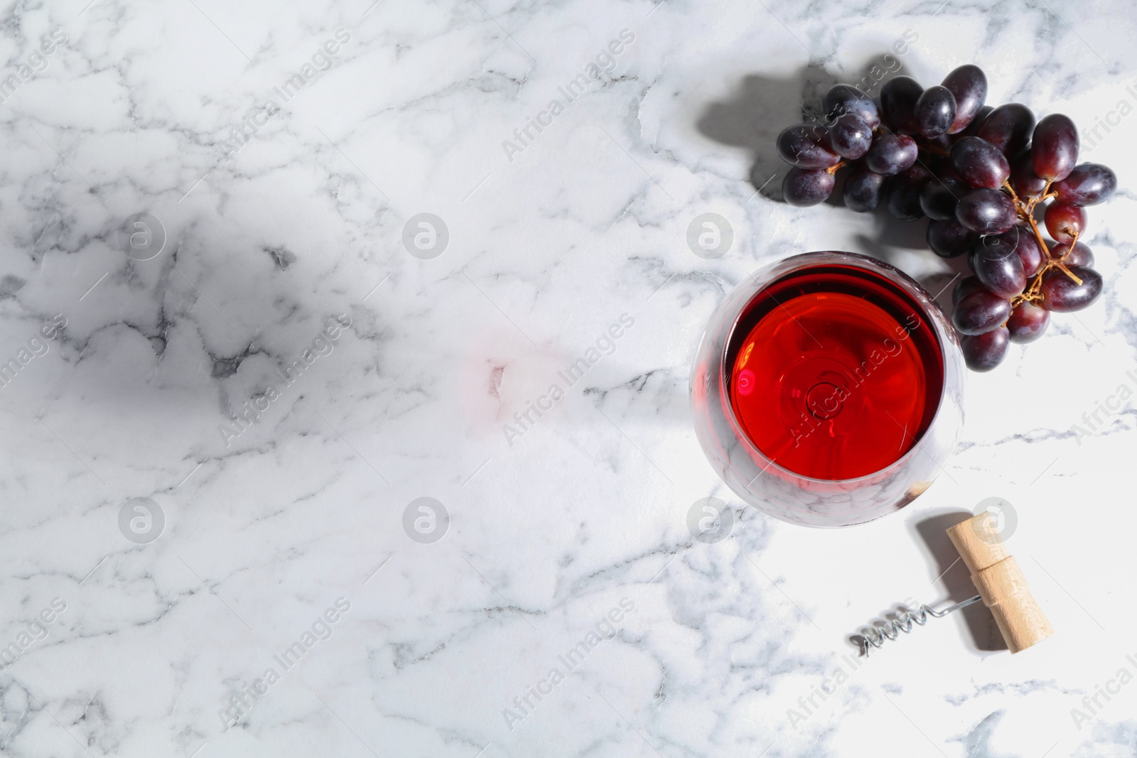 Photo of Corkscrew, glass of wine and grapes on white marble table, flat lay. Space for text