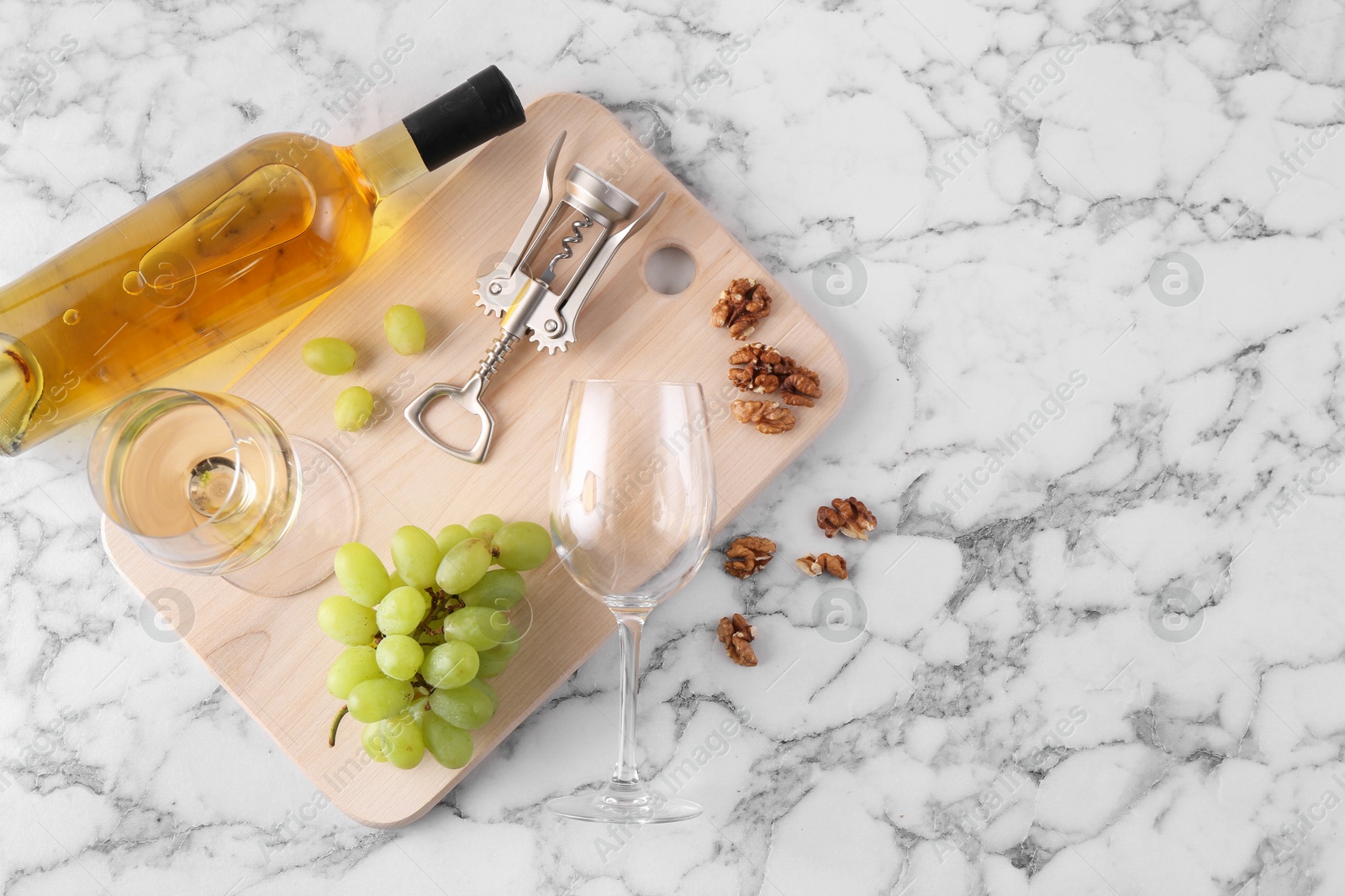 Photo of Wing corkscrew, bottle of wine, glasses, walnuts and grapes on white marble table, top view. Space for text