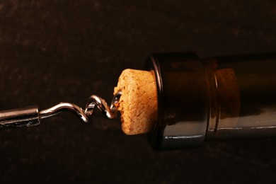 Wine bottle with corkscrew on dark background, closeup