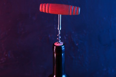 Wine bottle with corkscrew in lights on dark background, closeup