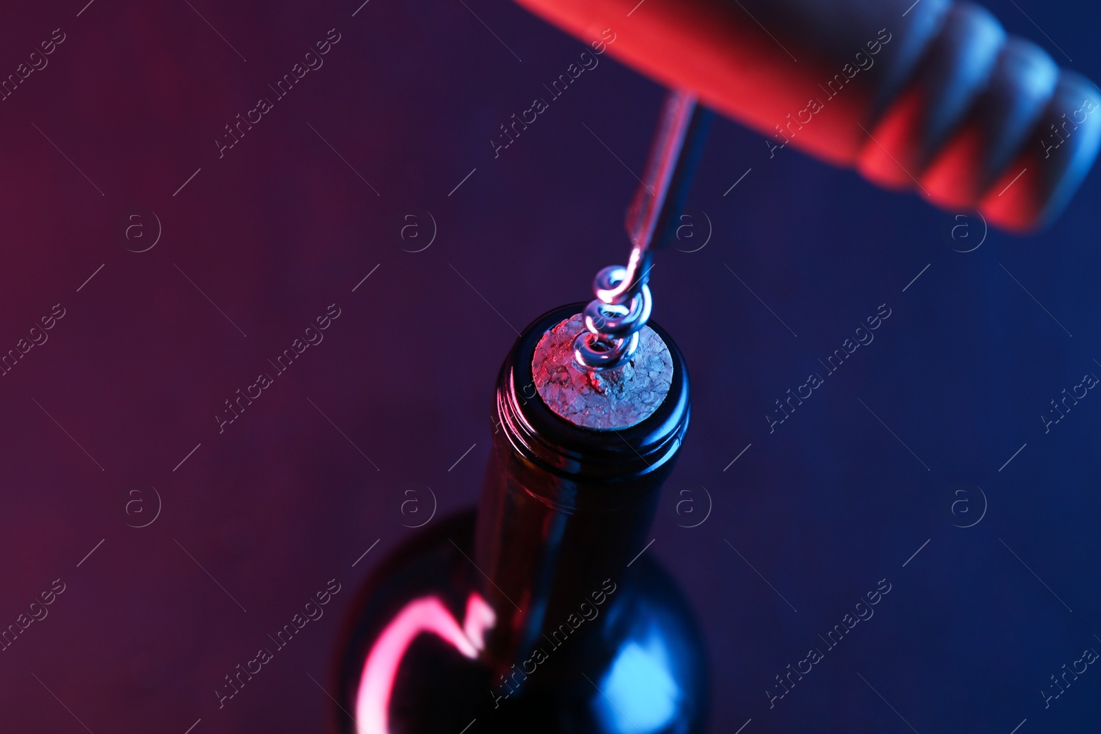 Photo of Wine bottle with corkscrew in lights on dark background, closeup