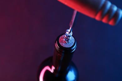 Photo of Wine bottle with corkscrew in lights on dark background, closeup