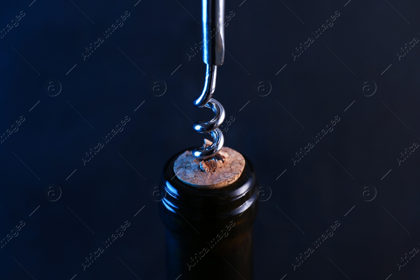 Photo of Wine bottle with corkscrew on dark background, closeup