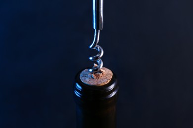 Photo of Wine bottle with corkscrew on dark background, closeup