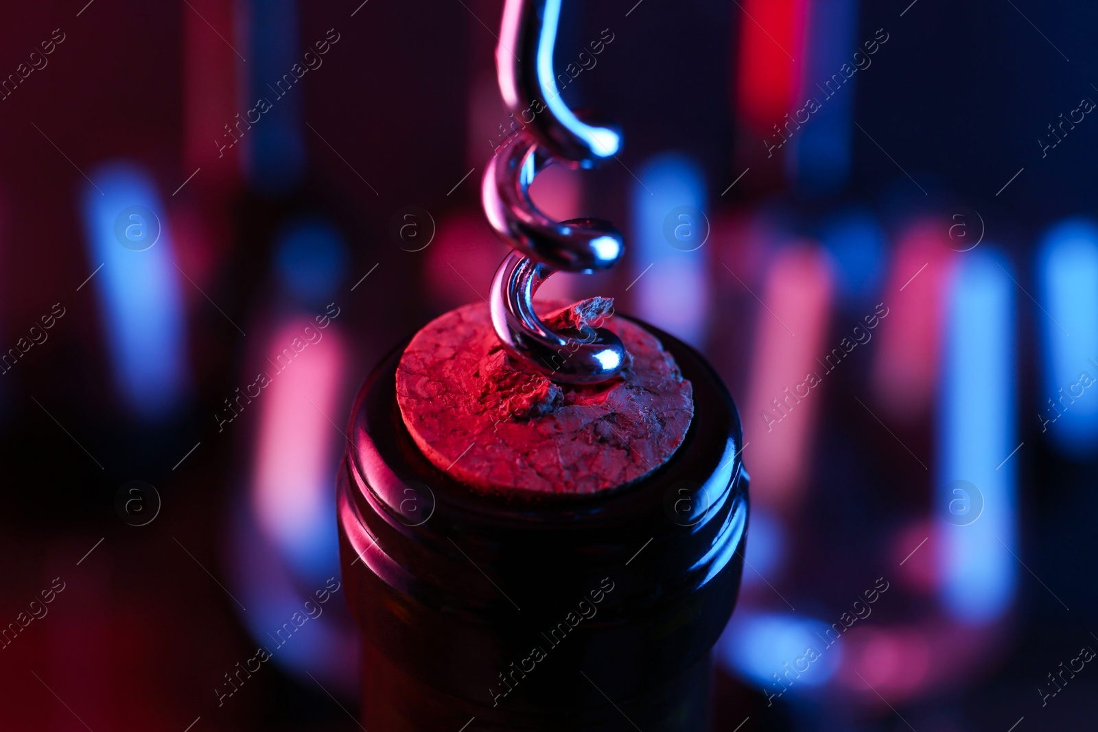 Photo of Wine bottle with corkscrew in lights on blurred background, closeup