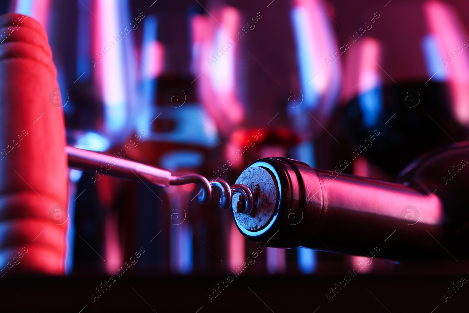 Photo of Wine bottle with corkscrew in lights on blurred background, closeup