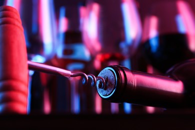 Photo of Wine bottle with corkscrew in lights on blurred background, closeup