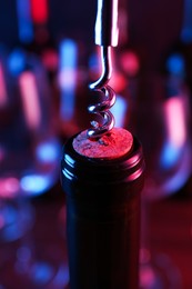 Photo of Wine bottle with corkscrew in lights on blurred background, closeup