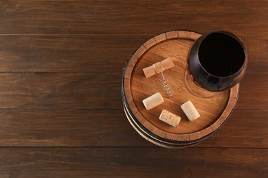 Photo of Corkscrew, corks, glass of wine and barrel on wooden, top view. Space for text