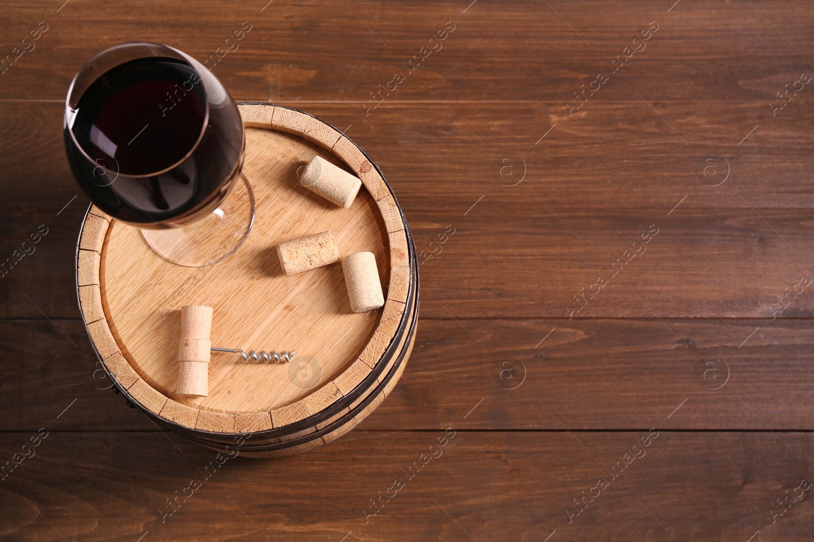 Photo of Corkscrew, corks, glass of wine and barrel on wooden, top view. Space for text