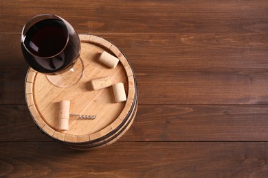 Photo of Corkscrew, corks, glass of wine and barrel on wooden, top view. Space for text