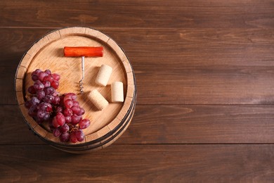 Photo of Corkscrew, corks, grapes and barrel on wooden table, top view. Space for text