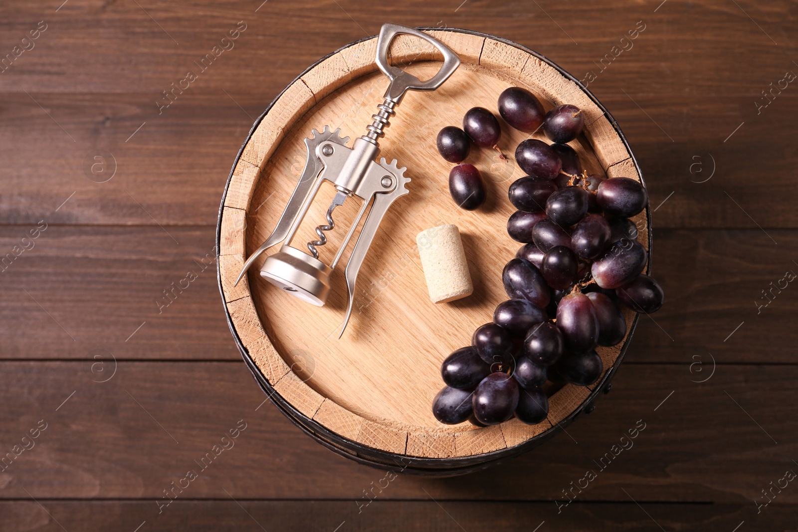 Photo of Wing corkscrew, cork, grapes and barrel on wooden table, top view