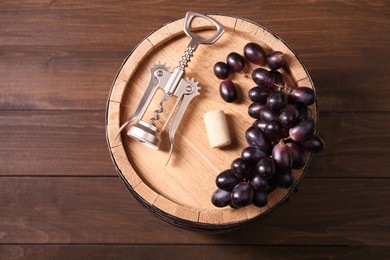 Photo of Wing corkscrew, cork, grapes and barrel on wooden table, top view