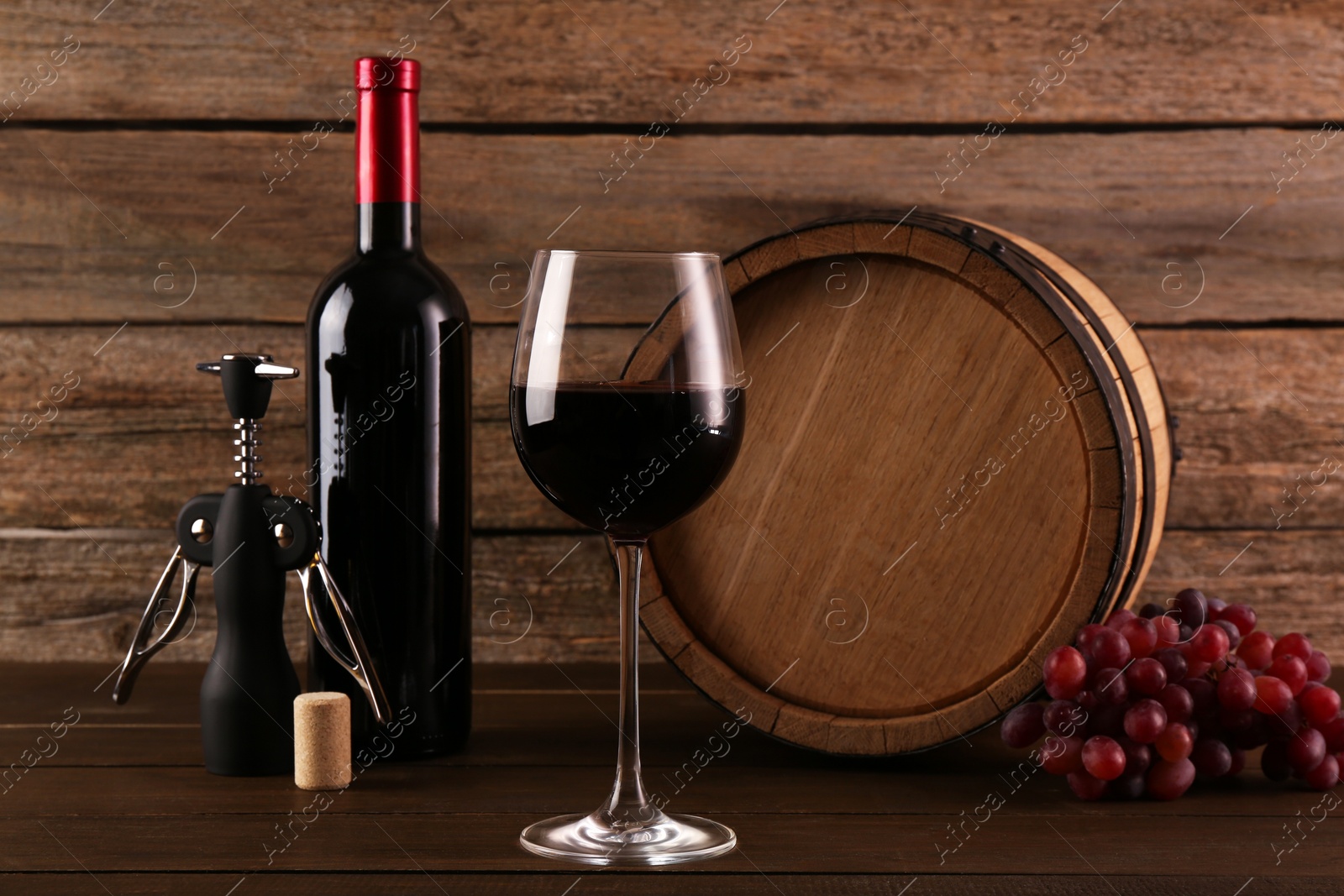 Photo of Glass of wine, bottle, wing corkscrew, barrel and grapes on wooden table