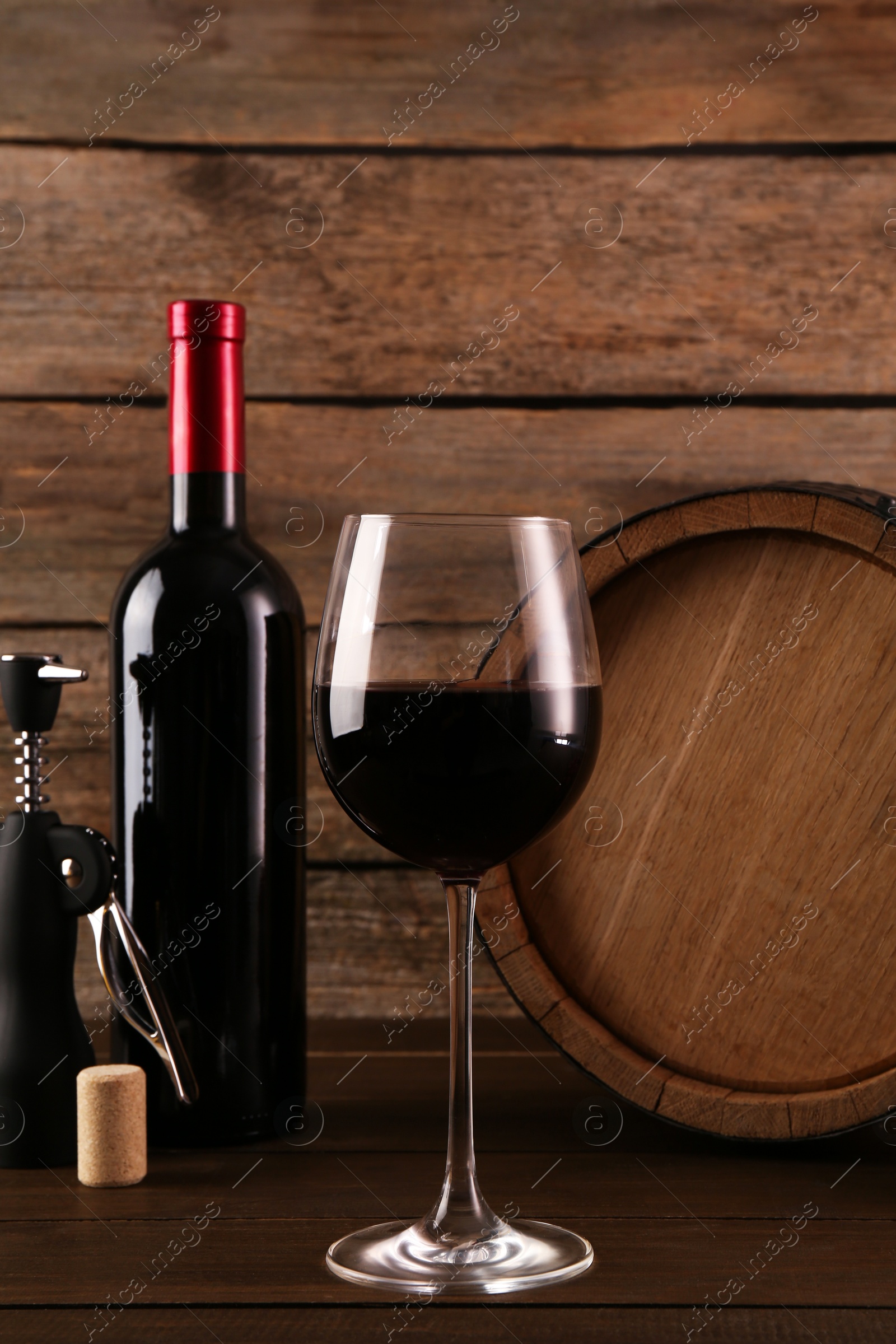 Photo of Glass of wine, bottle, wing corkscrew and barrel on wooden table