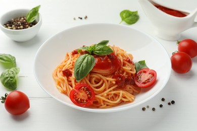 Photo of Delicious pasta with tomato sauce, peppercorns, vegetables and basil on white wooden table