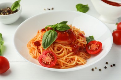 Photo of Delicious pasta with tomato sauce, peppercorns, vegetables and basil on white wooden table, closeup