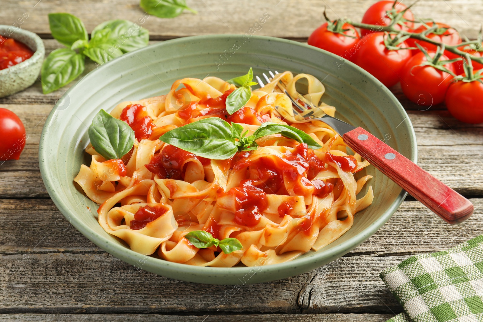 Photo of Delicious pasta with tomato sauce, basil and fork in bowl on wooden table, closeup