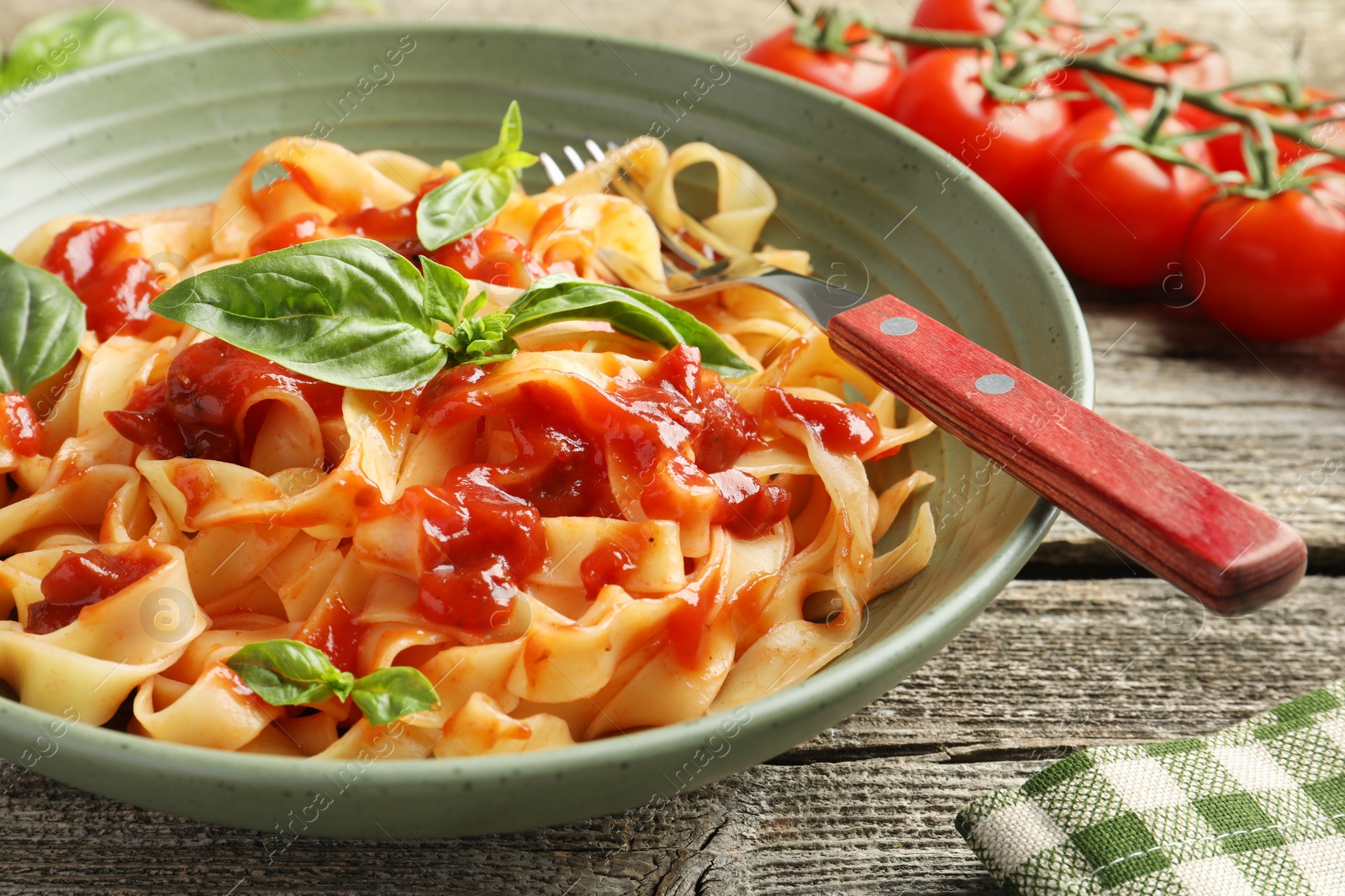 Photo of Delicious pasta with tomato sauce, basil and fork in bowl on wooden table, closeup