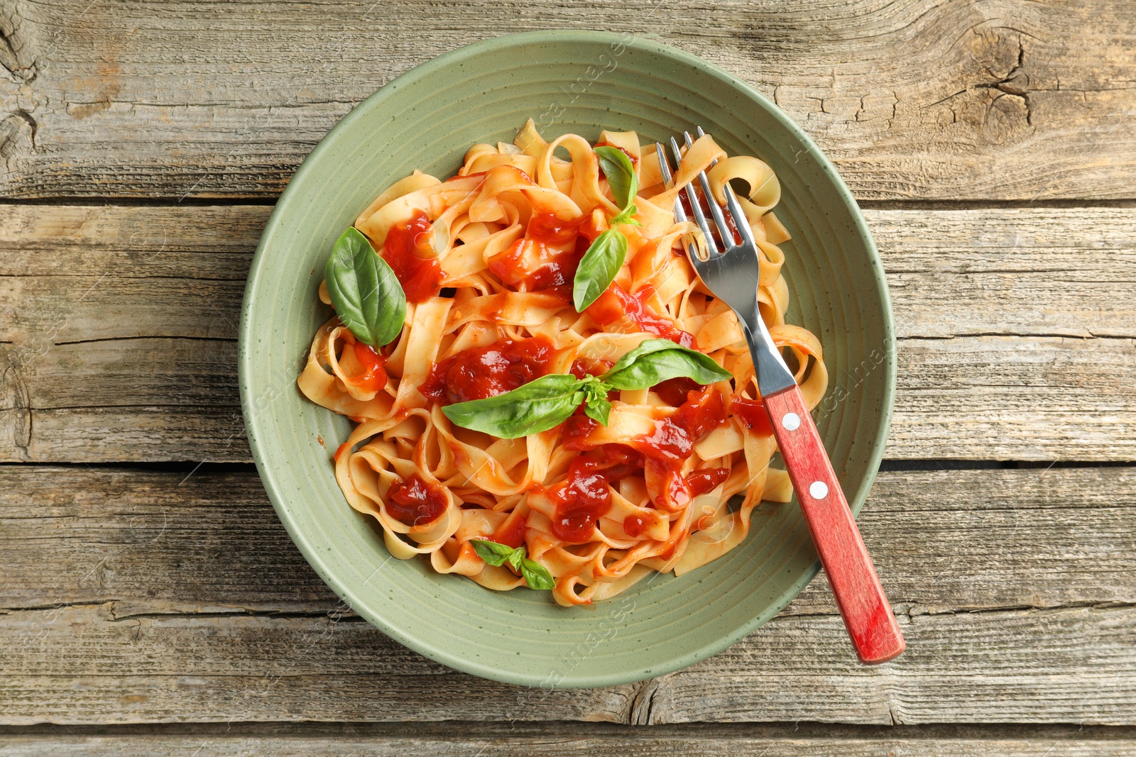 Photo of Delicious pasta with tomato sauce and basil in bowl on wooden table, top view