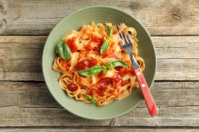 Photo of Delicious pasta with tomato sauce and basil in bowl on wooden table, top view